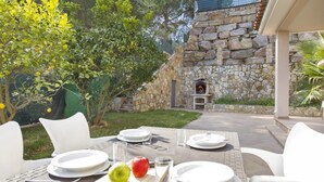 An outdoor dining area with white chairs and tables, a stone wall, and a stone fireplace. - Vila Lina in Lloret de Mar (Lloret de Mar)