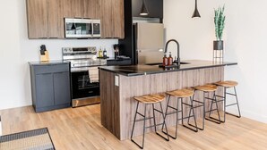 Una cocina moderna con armarios de madera, electrodomésticos de acero inoxidable, una isla central con taburetes altos e iluminación colgante.