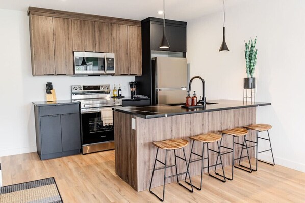 A modern kitchen with wooden cabinets, stainless steel appliances, a central island with bar stools, and pendant lighting.
