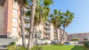 Un edificio residencial de varios pisos con balcones, palmeras y un césped bien cuidado.
