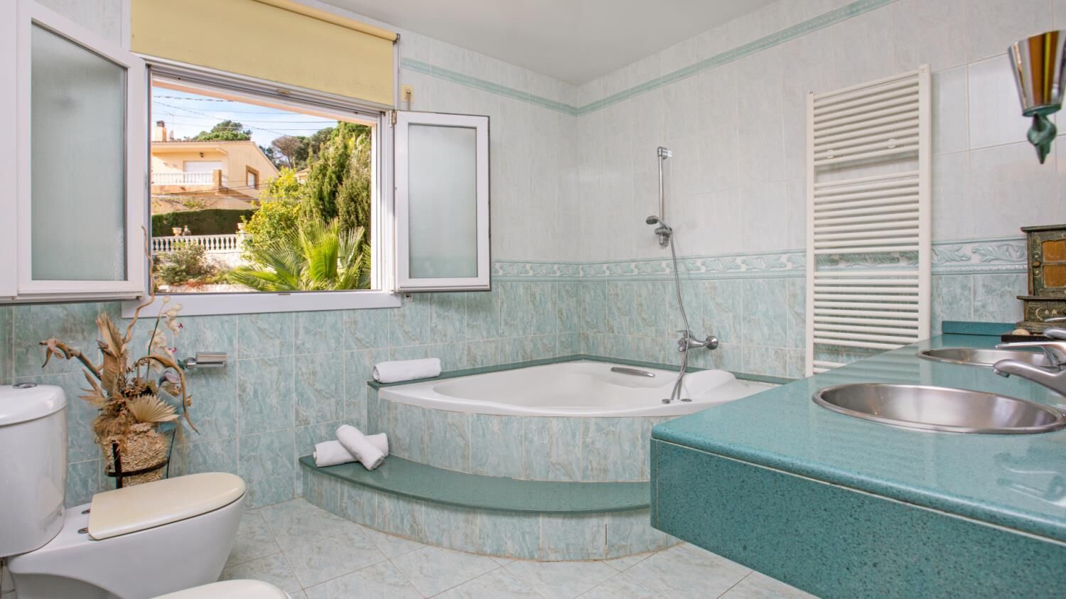 A bathroom with a bathtub, a toilet, a sink, and a window with a view of greenery.