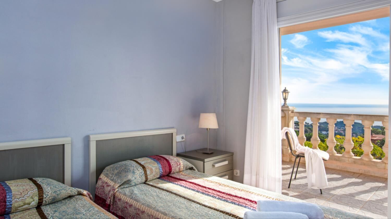 Camera d'albergo con due letti, un comodino, una lampada e un balcone con vista sul mare.