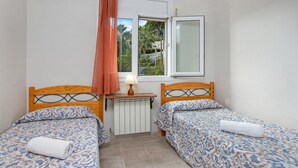 Une petite pièce avec deux lits, une fenêtre donnant sur un espace verdoyant, un radiateur et une lampe.