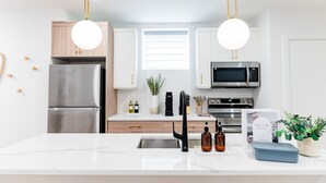 Une cuisine moderne avec des armoires blanches, des appareils en acier inoxydable et des luminaires suspendus.