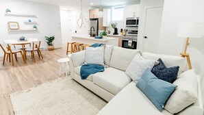 Un salon moderne avec un canapé, une table à manger et des chaises, et un coin cuisine à l’arrière-plan.
