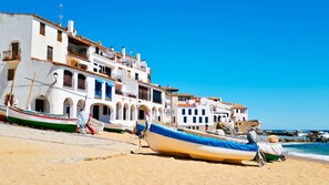 A coastal building with multiple balconies and arches, boats on the beach, and a clear blue sky. - Vila Albo in Calella de Palafrugell (Palafrugell)