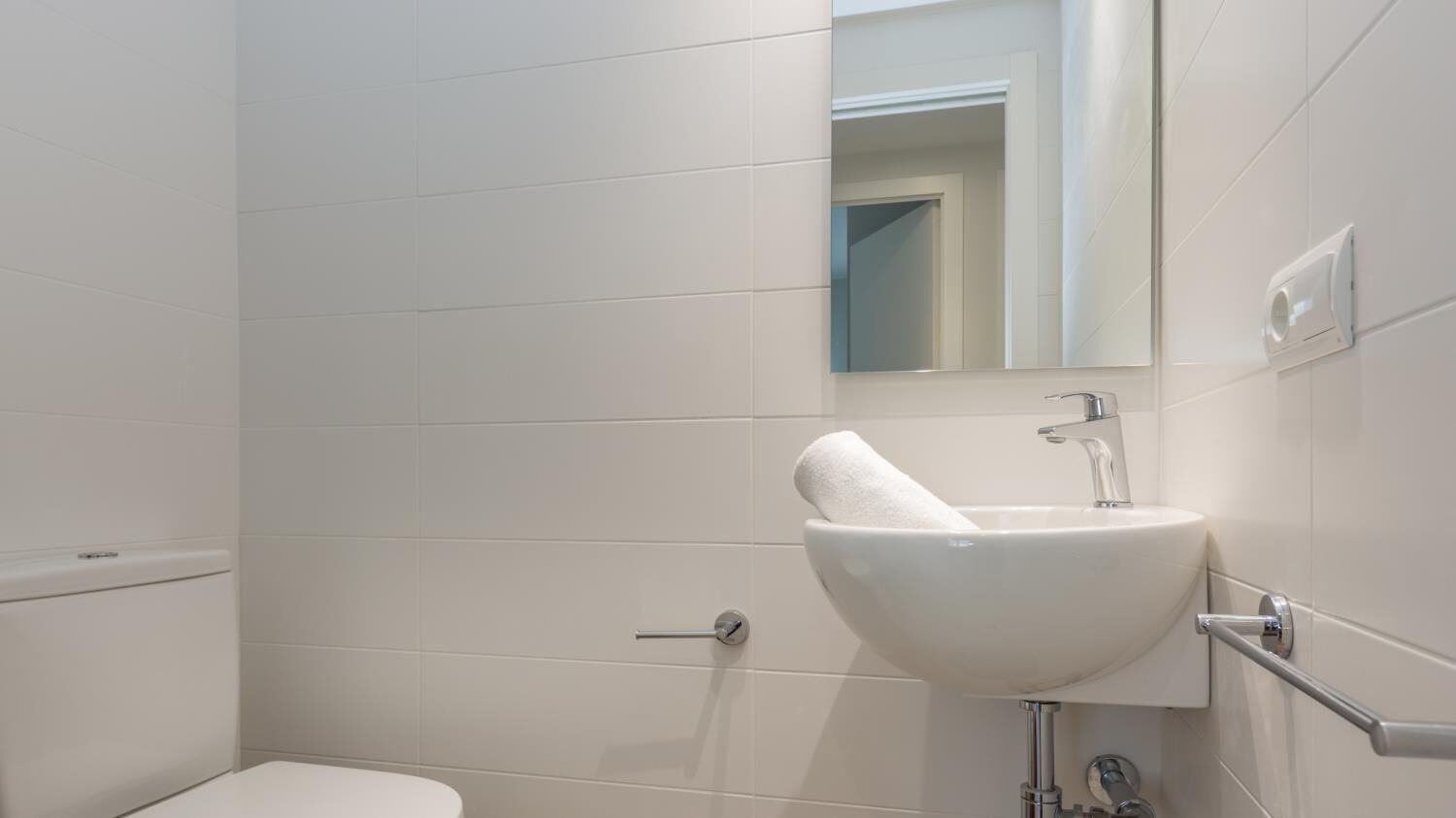 A modern bathroom with a white sink, a mirror, and a toilet.