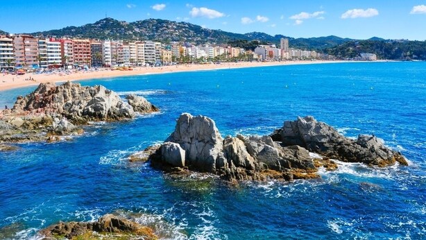 Un paysage urbain côtier avec une plage, des affleurements rocheux et une rangée d’immeubles à plusieurs étages.