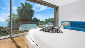 Une chambre dotée d’une grande porte-fenêtre coulissante donnant sur un balcon avec vue sur les palmiers et l’océan.