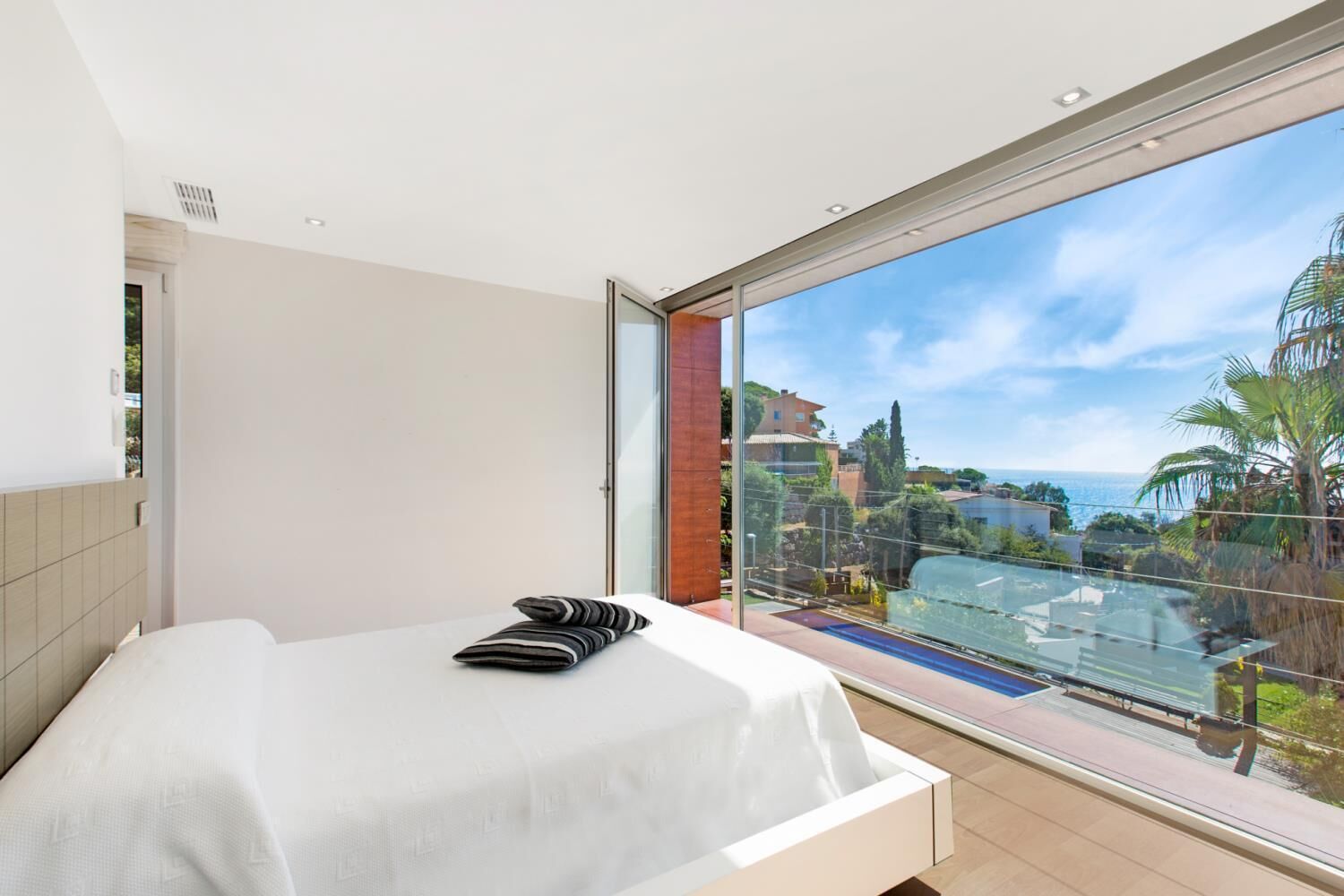 A bedroom with a large window overlooking a pool and a view of buildings and trees.