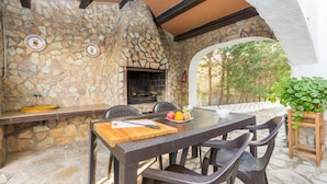 Cocina exterior con paredes de piedra, una parrilla y una mesa de comedor con sillas.