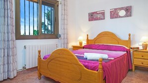Un dormitorio con una cama de madera, dos mesitas de noche, un ventanal con cortinas y dos obras de arte colgadas en la pared.