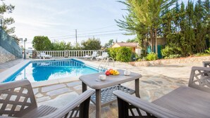 Una piscina con sillas de descanso y una mesa con frutas y una taza.