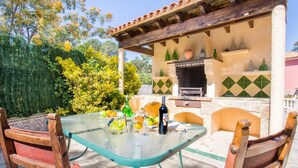 Un patio exterior con una mesa de vidrio, sillas de madera y una parrilla.
