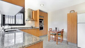 A modern kitchen with granite countertops, wooden cabinets, a built-in oven, microwave, and a dining area with a table and chairs. - Camelia in Llafranc With 4 Bedrooms and 3 Bathrooms (Vidreres)