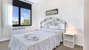 A bedroom with a bed, a window, a radiator, a nightstand, and a wall art piece. - Camelia in Llafranc With 4 Bedrooms and 3 Bathrooms (Vidreres)
