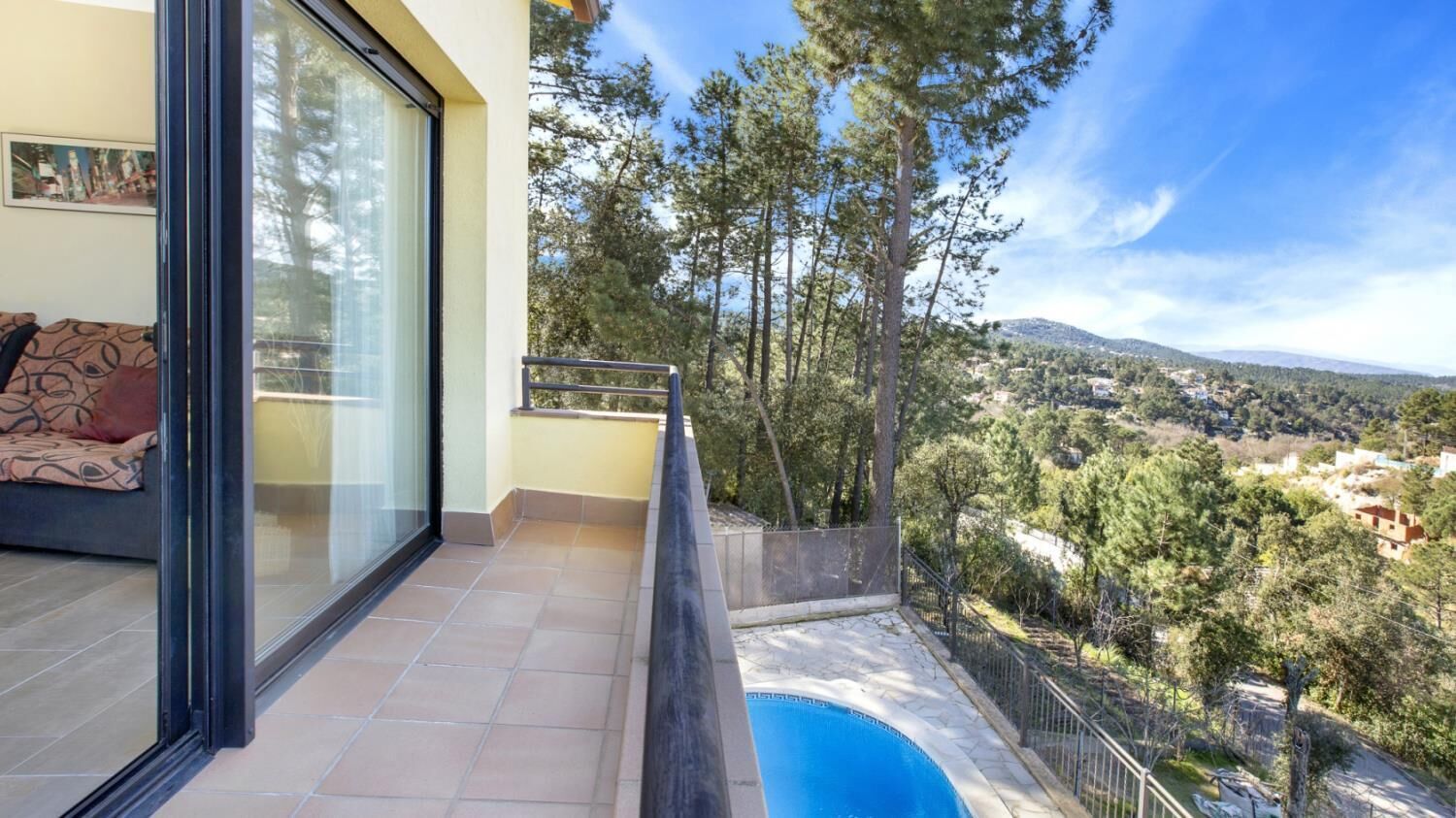 Un balcon avec une piscine, offrant une vue panoramique sur un paysage verdoyant, avec des arbres et des bâtiments situés au loin.