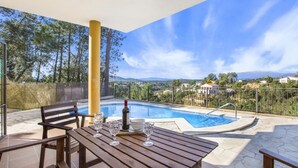 A poolside area with a table set for two, a bottle of wine, and a view of a mountain range. - Camelia in Llafranc With 4 Bedrooms and 3 Bathrooms (Vidreres)