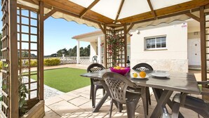 An outdoor patio with a table and chairs, a pergola, and a view of a white building with a garden. - Carolina in Vidreres (Vidreres)