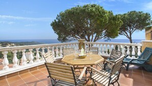 Una terraza con una mesa redonda de madera, cuatro sillas de madera y vista al mar.
