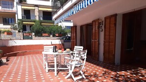 Une terrasse extérieure avec une table et des chaises, un sol carrelé et une vue sur un immeuble doté de balcons et de fenêtres.