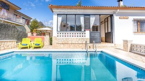 A pool area with a stone wall, a covered seating area, and a building with a tiled entrance.