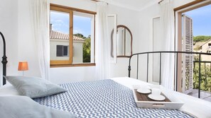 A bedroom with a bed, a bedside table, a window, and a balcony.