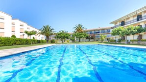 Une piscine à l’eau d’un bleu cristallin, entourée d’une végétation luxuriante et bien entretenue, ainsi que de bâtiments dotés de balcons.