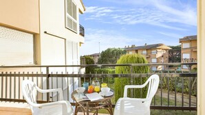 Un balcon avec deux chaises blanches, une petite table ronde et une vue sur les bâtiments voisins et la verdure.
