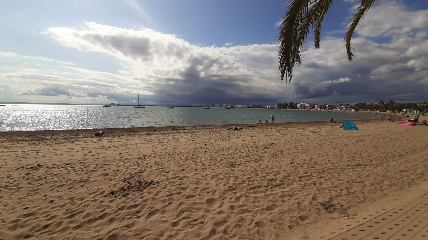 A beach with a sandy shore, a few people, and boats in the water.