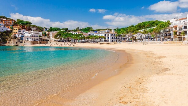 A beach with clear turquoise water, sandy shore, and buildings in the background. - Ronda in Llafranc With 4 Bedrooms and 3 Bathrooms (Palafrugell)