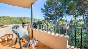 A balcony with a chair, a striped bag, and a view of a forested hillside and the sea. - Ronda in Llafranc With 4 Bedrooms and 3 Bathrooms (Palafrugell)