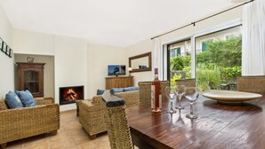 Una sala de estar acogedora con muebles de mimbre, una chimenea y un ventanal con vistas a la vegetación.