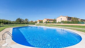 A swimming pool with a clear blue water, surrounded by a paved deck and a metal ladder. In the background, there are houses with red roofs and a well-maintained lawn. - Mas Pinell 44 in Vidreres (Torroella de Montgrí)