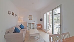 Una sala de estar con un sofá, una mesa y una silla. Hay un armario y un espejo en la pared.