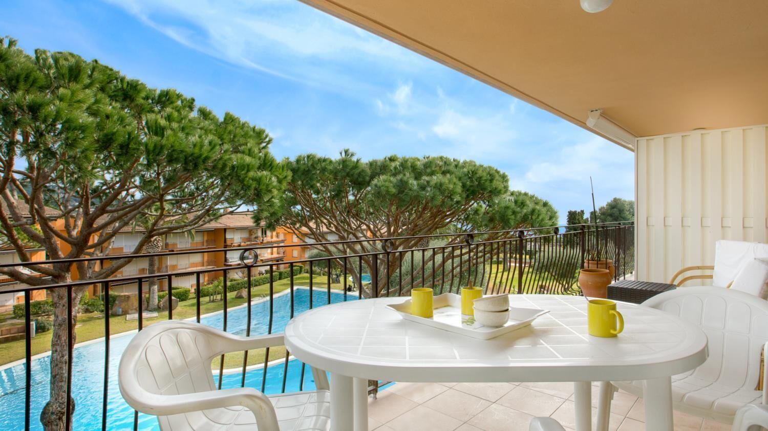 A balcony with a white table and chairs, overlooking a swimming pool and lush trees.