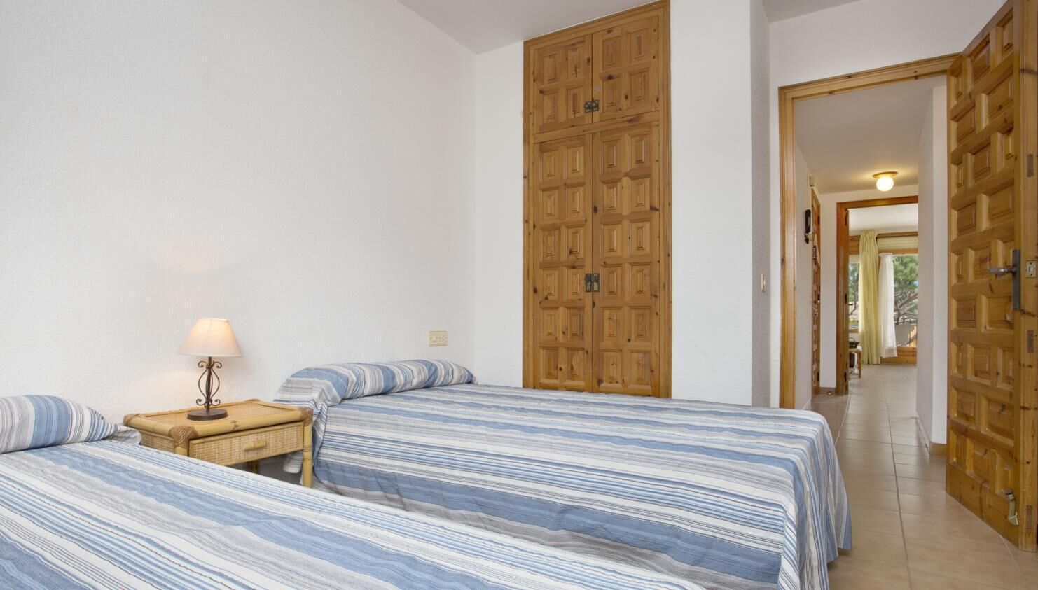 A bedroom with two beds, a nightstand, a lamp, and wooden wardrobes.