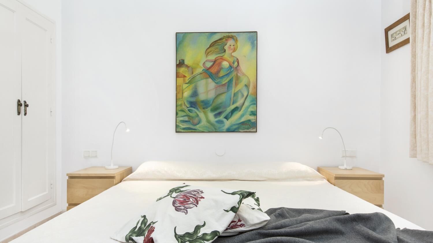 A bedroom with a bed, two bedside tables, a nightstand, a painting on the wall, and a door.