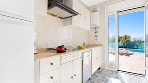 A modern kitchen with a built-in oven, a stove, and a sink. There is a window providing a view of a swimming pool and a patio area. - Alonso in Vidreres With 4 Bedrooms and 1 Bathrooms (Vidreres)