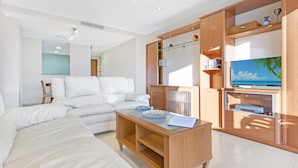 A modern living room with a white sofa, a wooden coffee table, and built-in shelving with a television and decorative items. - Santa Cristina in Lloret de Mar (Lloret de Mar)