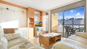 A modern living room with a sofa, a coffee table, and a TV. There is a sliding glass door leading to a balcony with a city view. - Santa Cristina in Lloret de Mar (Lloret de Mar)