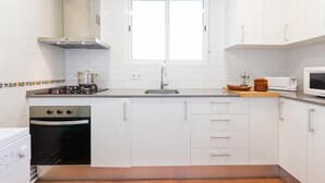 A modern kitchen with white cabinets, a stove, oven, microwave, and a window above the sink. - Pandora 1 in Llafranc (Palafrugell)