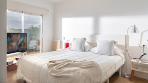 A modern bedroom with a large bed, a bedside table with a lamp, and a TV on the left. - Ferran in Llafranc With 4 Bedrooms and 2 Bathrooms (Palafrugell)