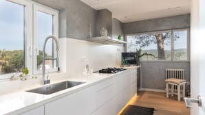 A modern kitchen with a large window, white cabinetry, a built-in stove, and a view of trees and hills. - Ferran in Llafranc With 4 Bedrooms and 2 Bathrooms (Palafrugell)