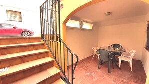 A staircase leading to a dining area with a table and chairs, a car parked outside, and a building with a barred window. - Pelegrins PL in Llafranc (Palafrugell)