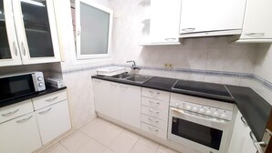 A kitchen with white cabinets, a black countertop, a microwave, a sink, and an oven. - Pelegrins PL in Llafranc (Palafrugell)