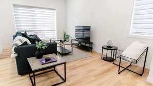 A modern living room with a sofa, coffee table, TV, and a side table with a plant. - Perfect Comfy Retreat | Premium Location Home Stay (Winnipeg)