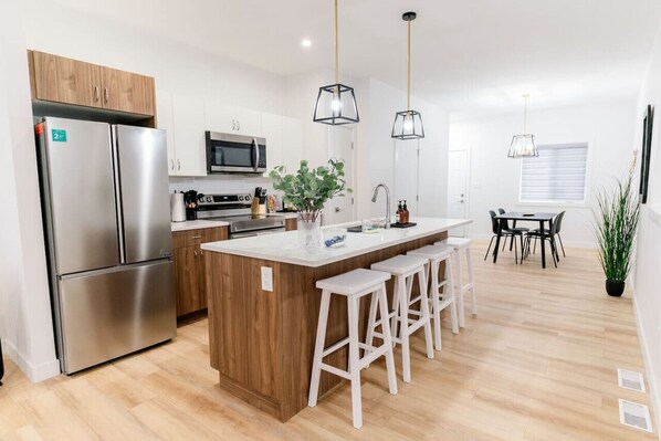 A modern kitchen with a central island, stainless steel appliances, and pendant lighting.