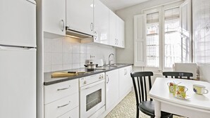 A modern kitchen with white cabinets, a built-in oven, and a dining area with a table and chairs. - Peral in Llafranc With 2 Bedrooms and 2 Bathrooms (Palafrugell)