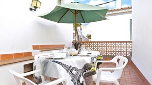 A table set for two with a green umbrella, white chairs, and a tablecloth featuring a cityscape design. - Peral in Llafranc With 2 Bedrooms and 2 Bathrooms (Palafrugell)